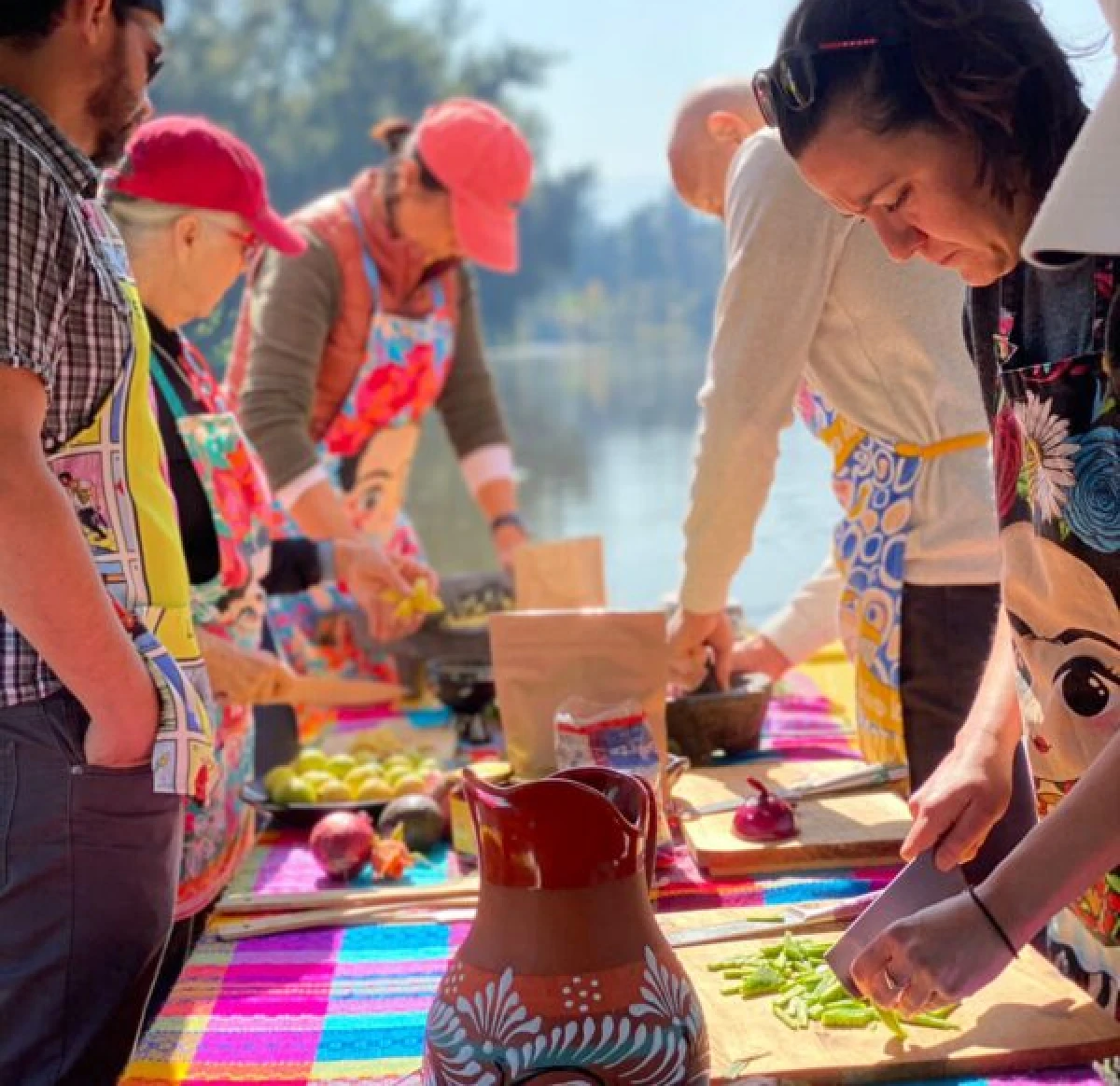 Group preparing a meal together at a corporate culinary experience by Mexico Foodie Tours, chopping fresh ingredients on a colorful table beside a Xochimilco canal.