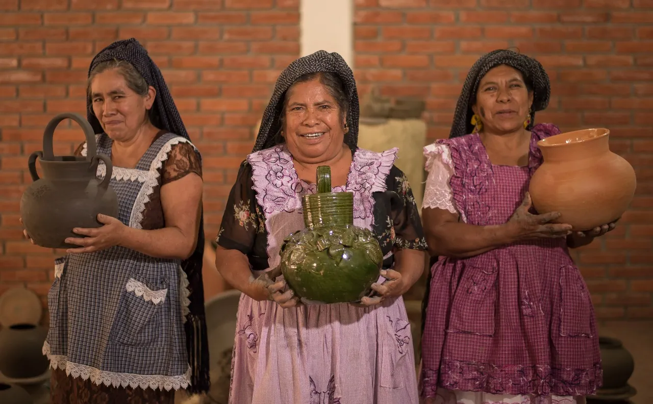 Three Oaxacan women artisans holding handmade clay pottery, including green glazed Atzompa ceramics, on an Oaxaca artisan tour by Mexico Foodie Tours